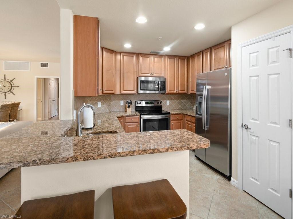 9118 Prima Way, Unit 101 Naples, FL 34113 - Photo 8 of 22 a kitchen with stainless steel appliances granite countertop a refrigerator a stove a sink and a microwave