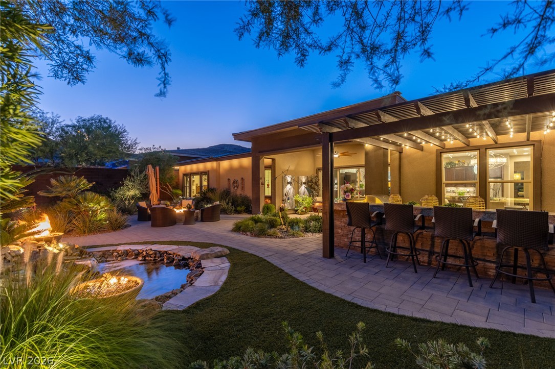10167 Copper Edge Road Las Vegas, NV 89148 - Photo 40 of 45 An inviting outdoor living space features a tranquil pond, fire bowls, and a bar area under a lighted pergola, perfect for evening gatherings.