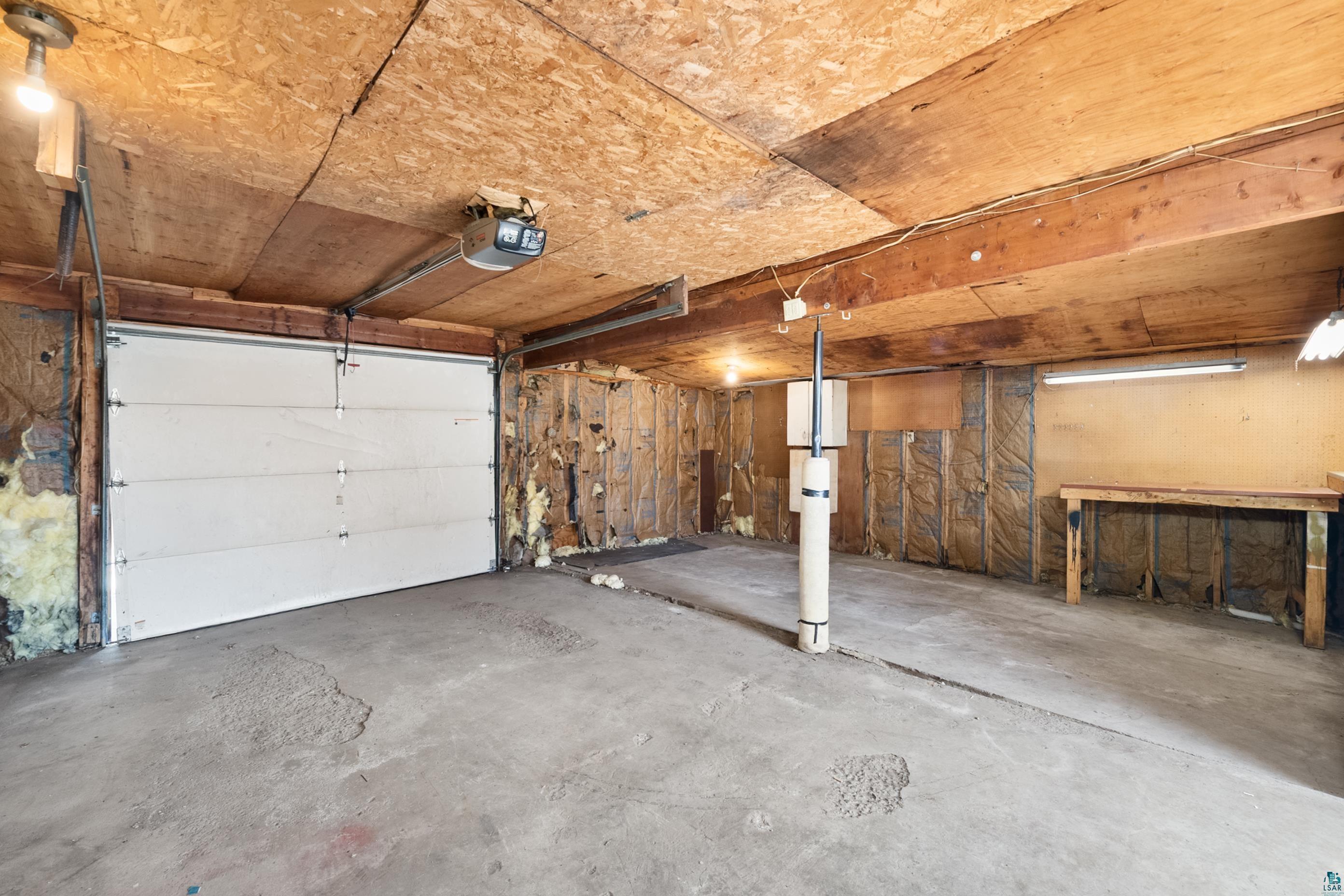 3067 Restormel Street Duluth, MN 55806 - Photo 23 of 25 Garage interior featuring a sectional overhead door with an automatic opener, exposed wood-finish ceiling, concrete flooring, and built-in work surface