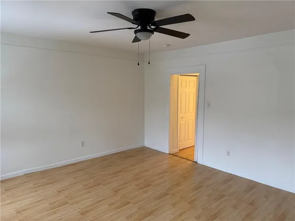 an empty room with wooden floor chandelier fan and windows