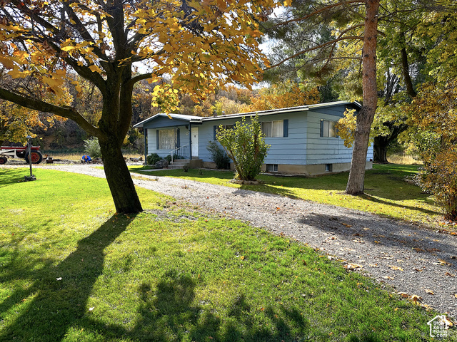 5035 South Hollow Road Logan, UT 84321 - Photo 2 of 19 Single-story residence featuring light blue siding, a covered entry with white railings, a gravel driveway, and mature trees with autumn foliage