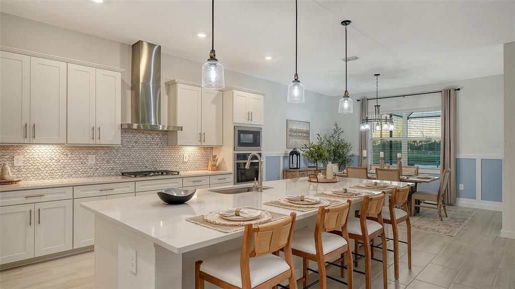 5612 Lightning Whelk Lane Lakewood Ranch, FL 34211 - Photo 20 of 44 a kitchen with stainless steel appliances kitchen island granite countertop a table chairs sink and cabinets