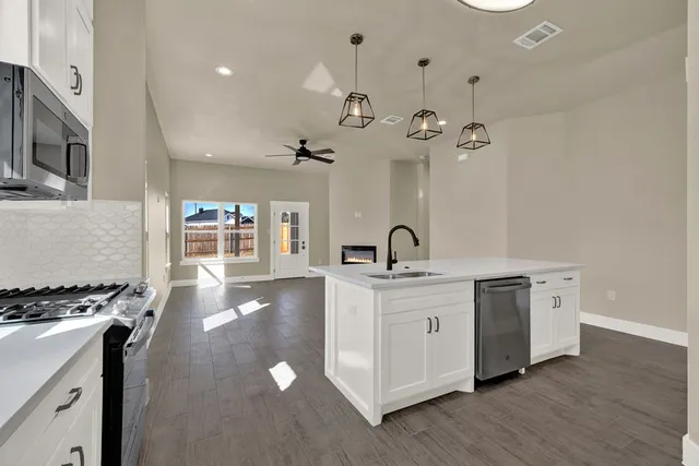 a open kitchen with stainless steel appliances a stove a sink a center island with wooden floor and cabinets