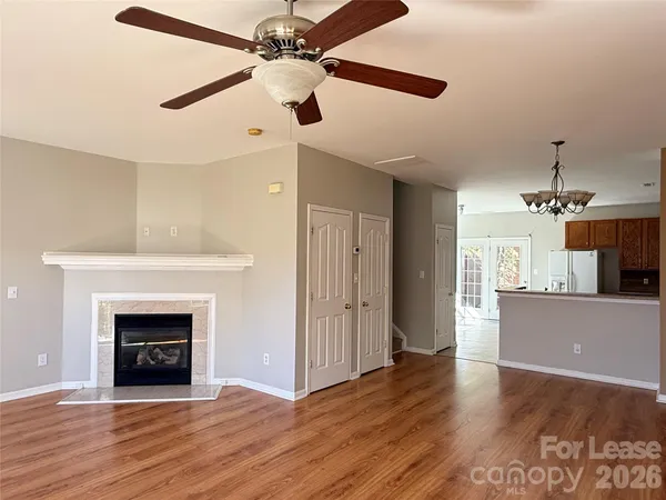 an empty room with wooden floor a ceiling fan a fireplace and windows