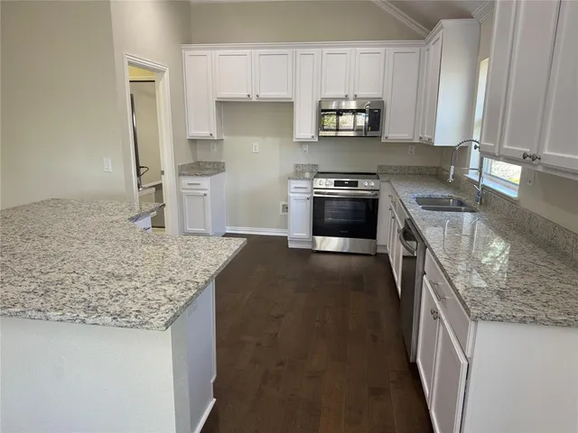 a kitchen with a sink dishwasher a stove and white cabinets with wooden floor