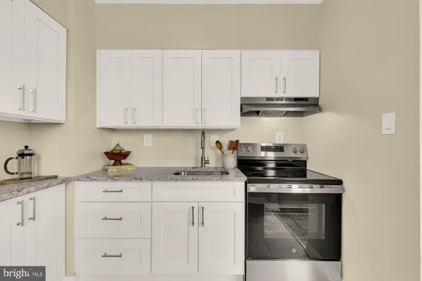 a kitchen with stainless steel appliances granite countertop a stove a sink and white cabinets