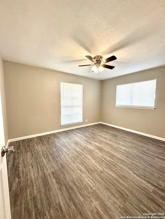 an empty room with wooden floor chandelier fan and windows
