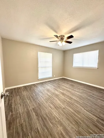 an empty room with wooden floor chandelier fan and windows