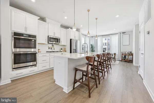 a kitchen with stainless steel appliances kitchen island granite countertop a stove a sink a microwave a refrigerator and white cabinets with wooden floor