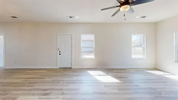 an empty room with wooden floor fan and windows