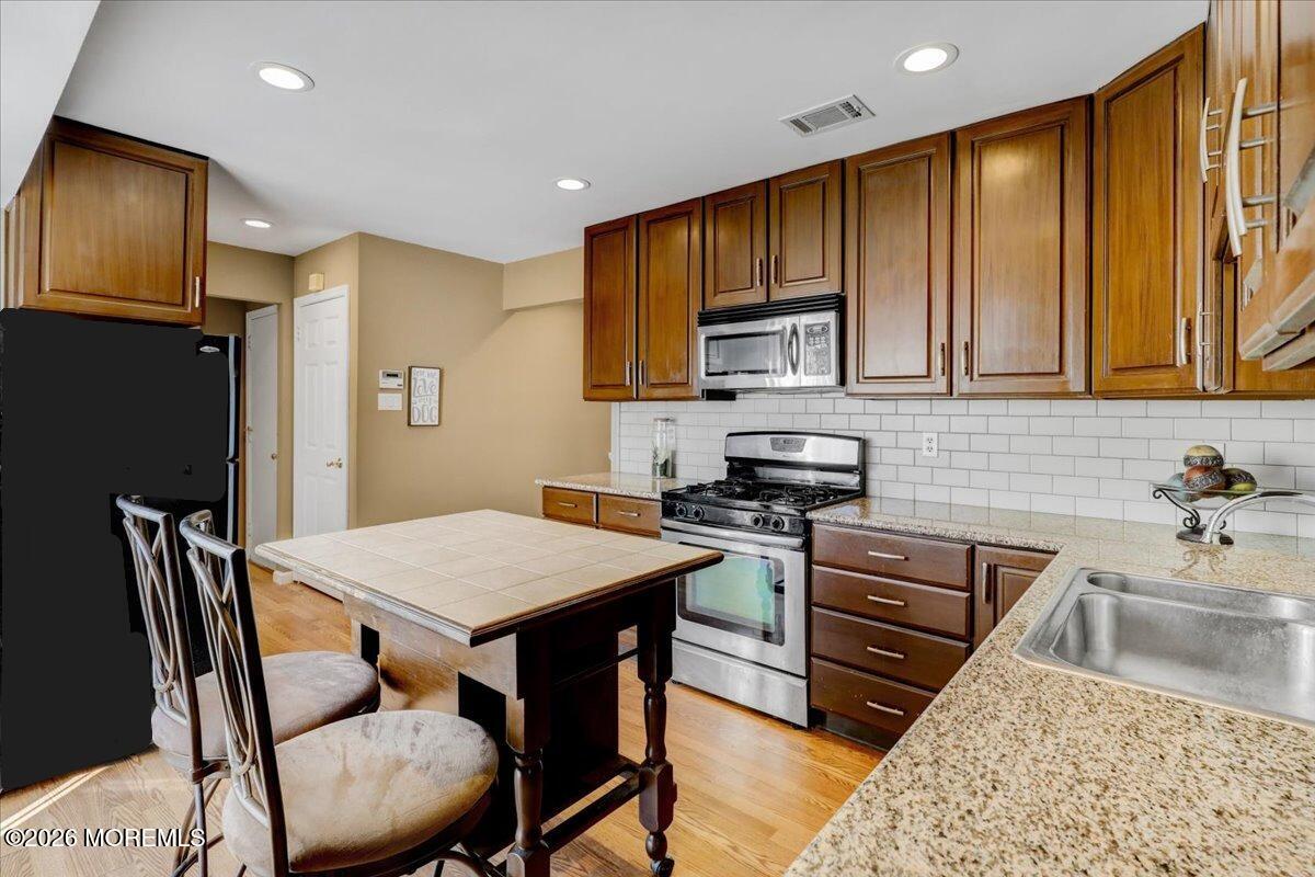 16 Regina Drive Howell, NJ 07731 - Photo 11 of 33 a kitchen with stainless steel appliances granite countertop a stove top oven a sink a refrigerator with a dining table and chairs