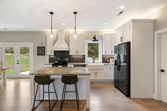 a kitchen with stainless steel appliances kitchen island granite countertop a refrigerator a stove a microwave oven a dining table and chairs with wooden floor