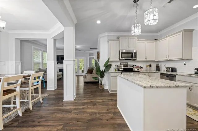 a kitchen with stainless steel appliances granite countertop a stove top oven a sink dishwasher a refrigerator and white cabinets with wooden floor