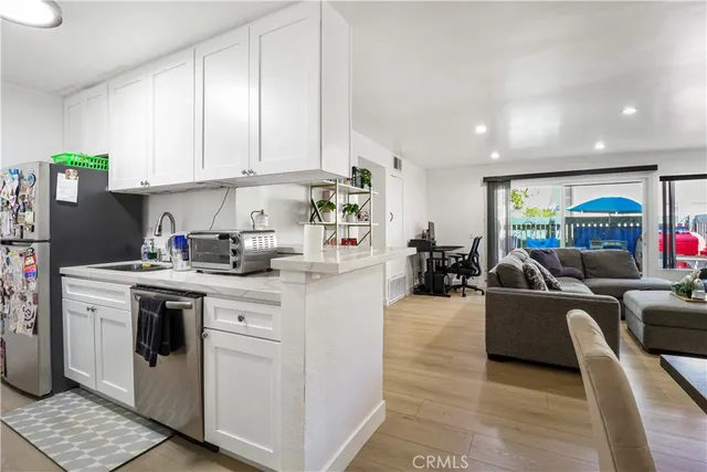 a kitchen with stainless steel appliances granite countertop a sink dishwasher stove refrigerator and couches with wooden floor