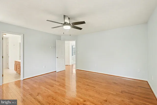 an empty room with wooden floor fan and windows