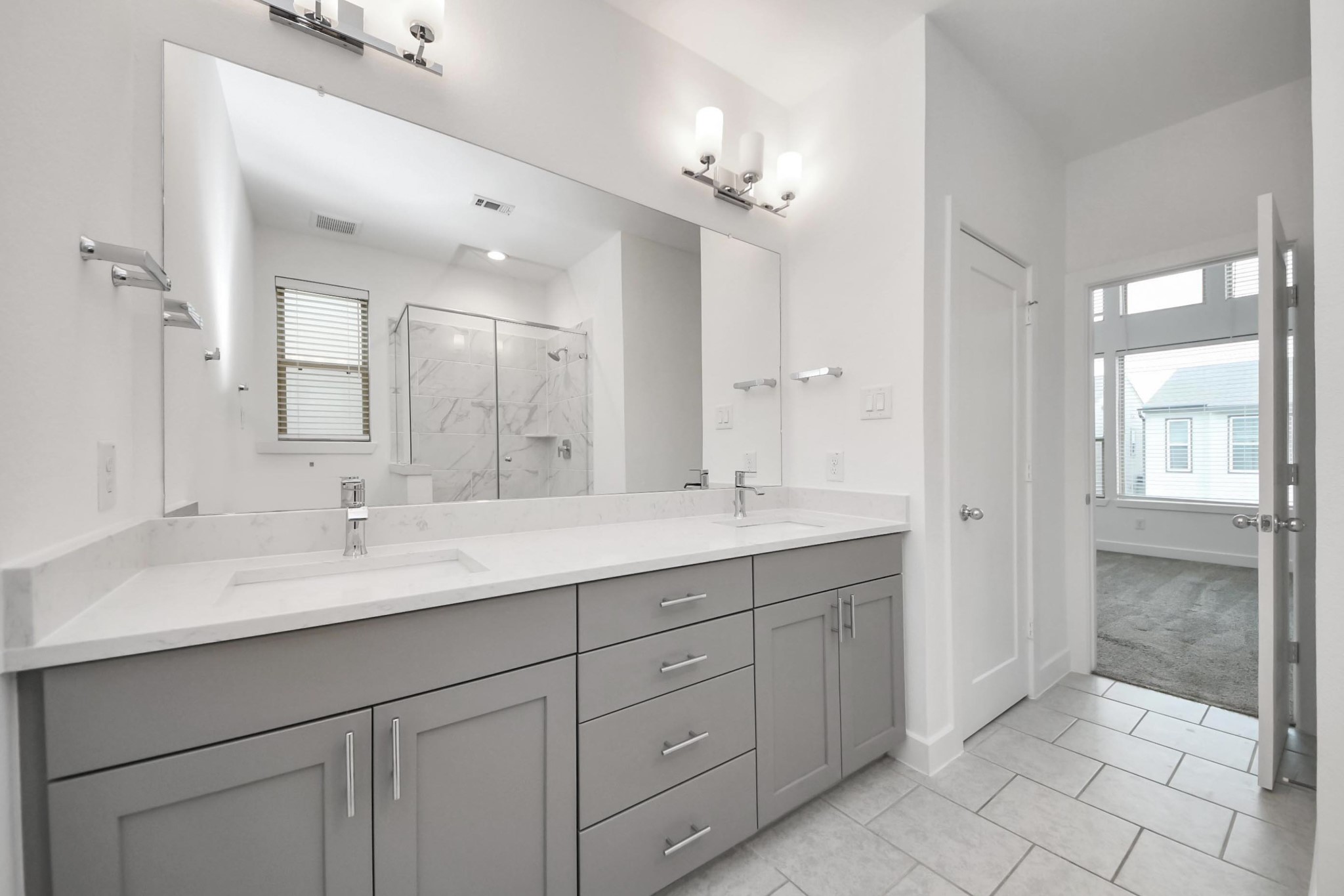18527 Centro Row Conroe, TX 77385 - Photo 29 of 44 The en-suite bathroom features an expansive dual-sink vanity and an equally wide mirror, perfectly complemented by a glass shower and soft gray tones.