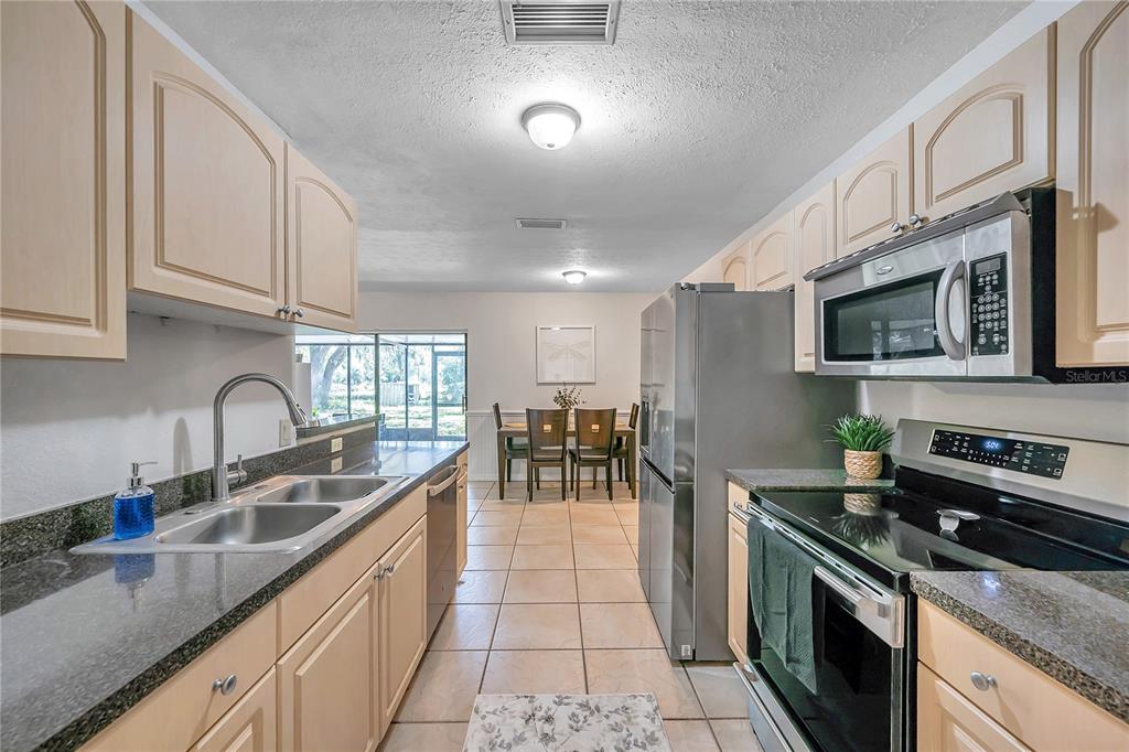 7405 Williams Road Seffner, FL 33584 - Photo 25 of 100 a kitchen with stainless steel appliances granite countertop a sink a stove top oven a chimney cabinets and living room view