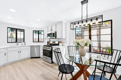 a kitchen with stainless steel appliances granite countertop a stove a sink a dining table and chairs with wooden floor