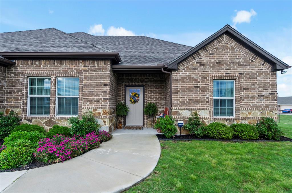 View of front facade featuring brick siding, roof with shingles, a front lawn, and stone siding