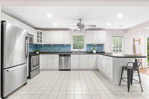 a kitchen with stainless steel appliances granite countertop a stove a sink dishwasher a refrigerator and white cabinets with wooden floor