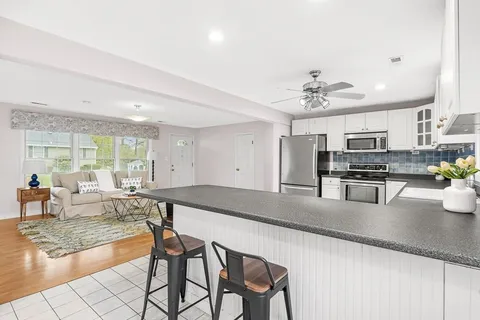 a kitchen with stainless steel appliances granite countertop a stove top oven a sink a dining table and chairs with wooden floor