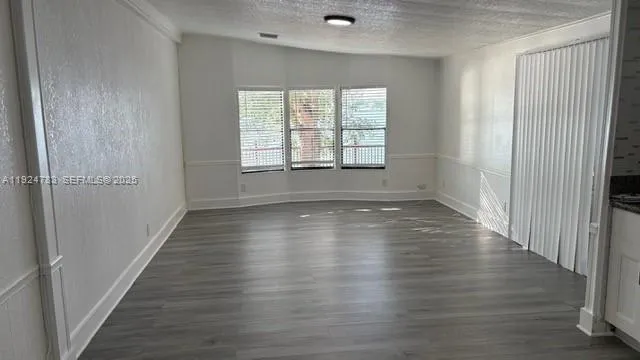 an empty room with wooden floor and windows with curtains
