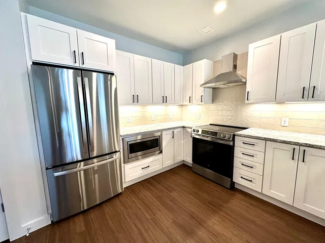 a kitchen with granite countertop a refrigerator stove and wooden cabinets