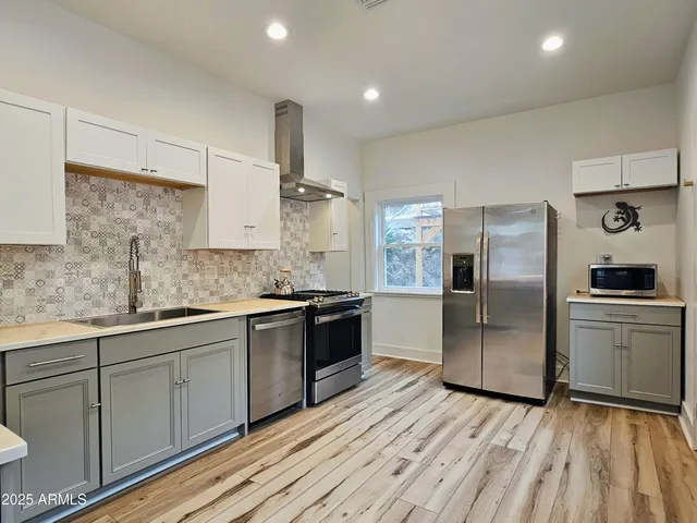 a kitchen with stainless steel appliances granite countertop a refrigerator a sink dishwasher a stove and white countertops with wooden floor
