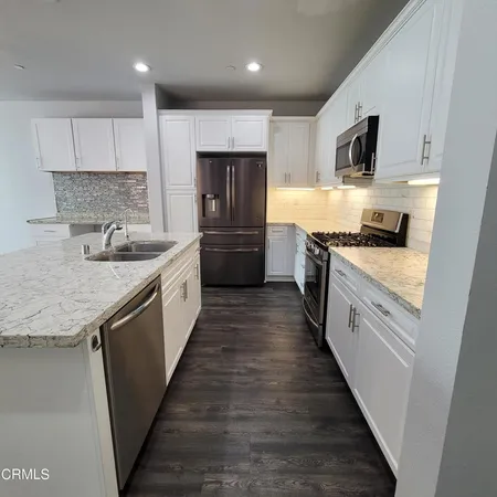 a kitchen with granite countertop kitchen island wooden floors appliances and white cabinets