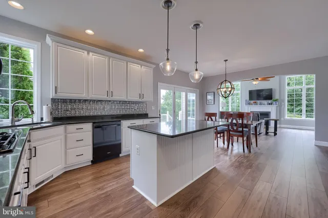 a kitchen with stainless steel appliances kitchen island granite countertop a stove a sink and white cabinets with wooden floor