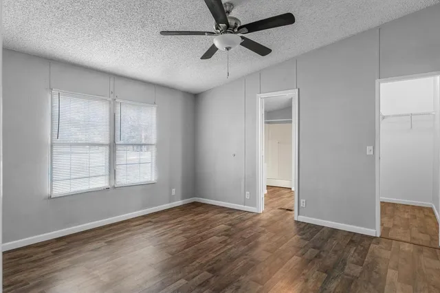 an empty room with wooden floor ceiling fan and windows
