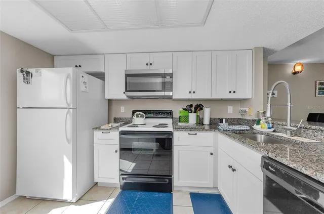 a kitchen with stainless steel appliances granite countertop a refrigerator stove a sink and white cabinets