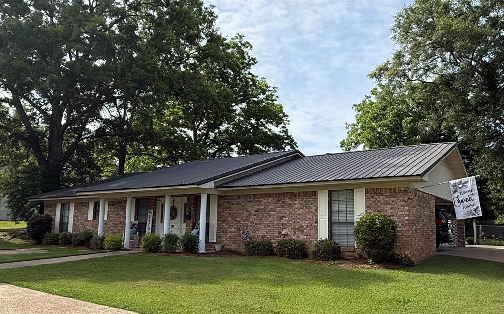 202 Butler Street Springhill, LA 71075 - Photo 1 of 2 Brick exterior with a dark metal roof, white columns, a manicured lawn, and mature trees