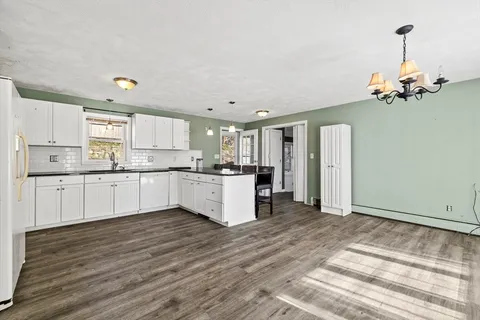 a large kitchen with kitchen island a stove a sink dishwasher a refrigerator and white cabinets with wooden floor