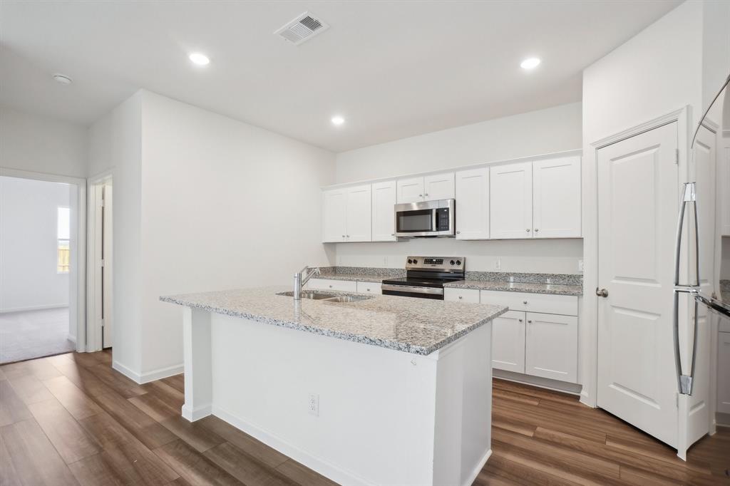 2104 Prairie Lane Melissa, TX 75454 - Photo 5 of 19 a kitchen with stainless steel appliances granite countertop a stove a sink a refrigerator a microwave and white cabinets with wooden floor