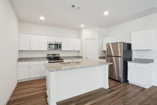 a kitchen with stainless steel appliances granite countertop a stove a sink a refrigerator a microwave and white cabinets with wooden floor