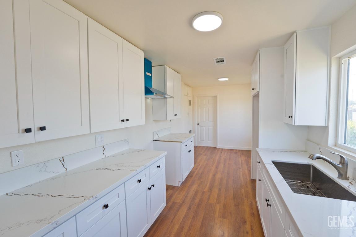 Undisclosed Address Bakersfield, CA 93308 - Photo 9 of 23 a kitchen with a sink dishwasher stove and white cabinets with wooden floor