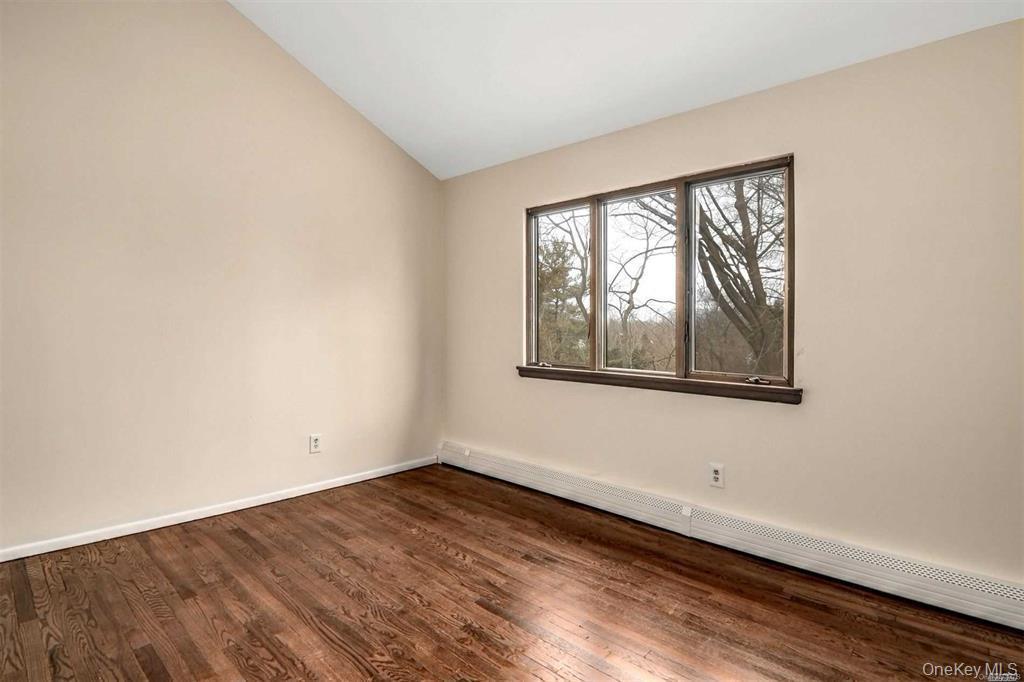 36 Bevin Road Northport, NY 11768 - Photo 17 of 26 Empty room with a baseboard heating unit, vaulted ceiling, and dark wood-style flooring