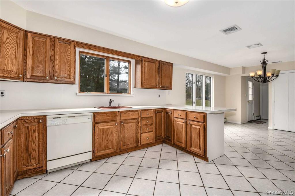 36 Bevin Road Northport, NY 11768 - Photo 5 of 26 Kitchen with a peninsula, brown cabinets, light countertops, dishwasher, and hanging light fixtures