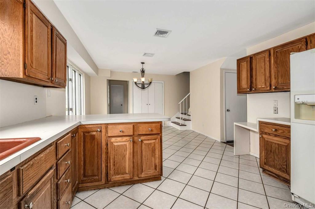 36 Bevin Road Northport, NY 11768 - Photo 6 of 26 Kitchen with brown cabinetry, light countertops, a chandelier, and white fridge with ice dispenser