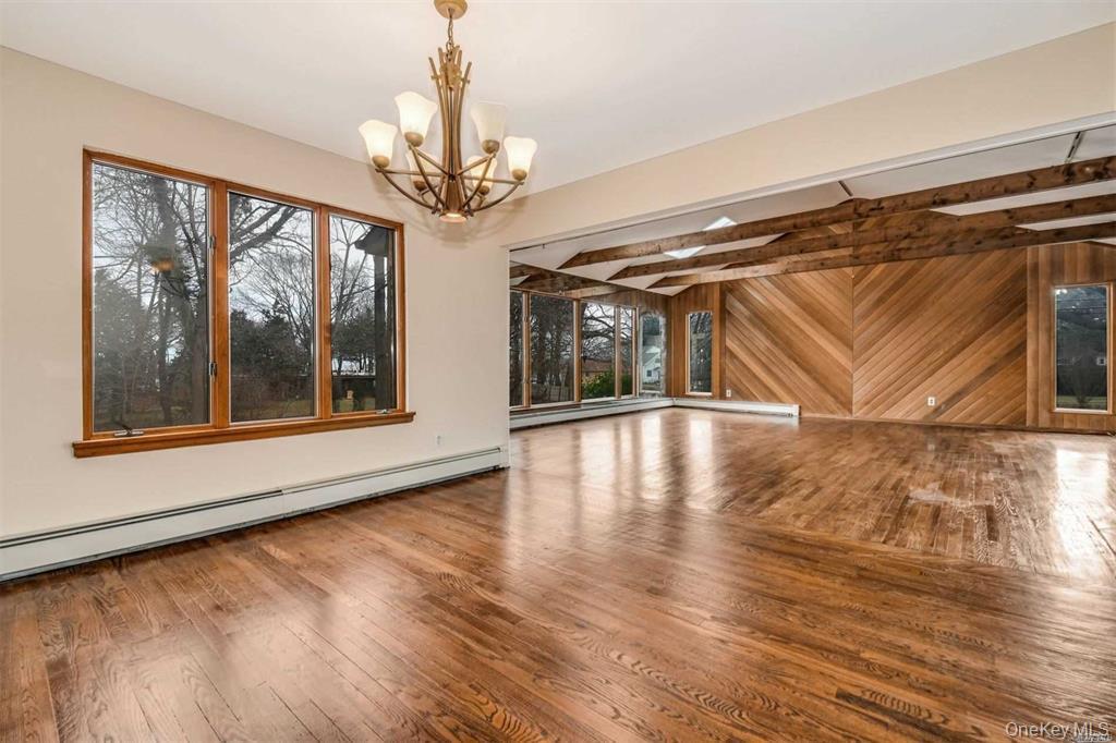 36 Bevin Road Northport, NY 11768 - Photo 8 of 26 Unfurnished living room featuring baseboard heating, hardwood / wood-style floors, wood walls, a chandelier, and beam ceiling