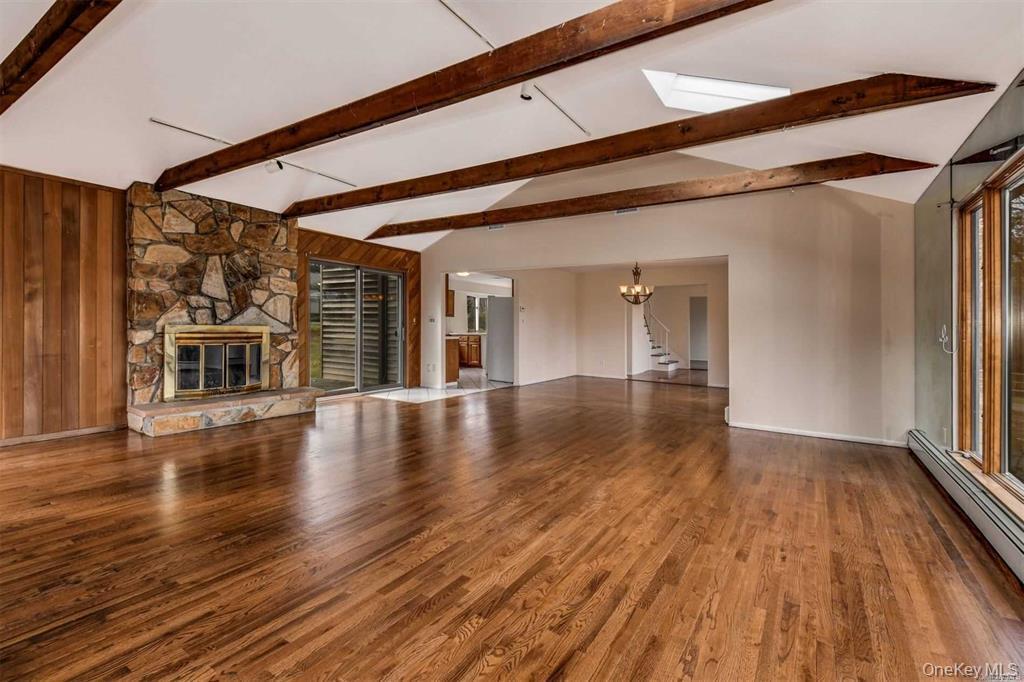 36 Bevin Road Northport, NY 11768 - Photo 9 of 26 Unfurnished living room with a stone fireplace, wood finished floors, a baseboard radiator, wood walls, and stairway