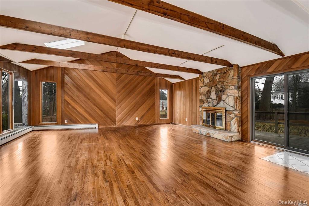 36 Bevin Road Northport, NY 11768 - Photo 10 of 26 Unfurnished living room featuring wooden walls, wood finished floors, plenty of natural light, and a fireplace