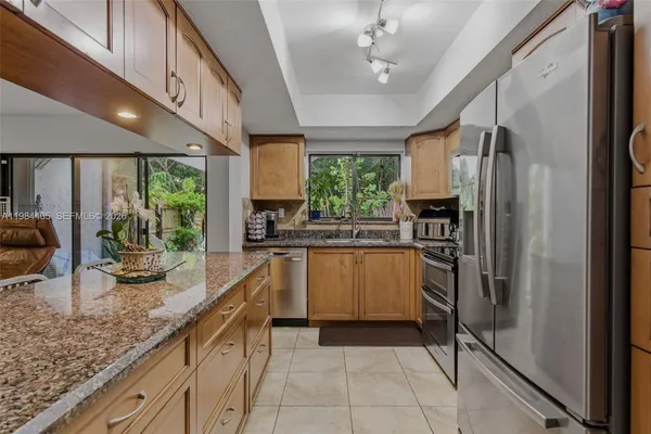 a kitchen with stainless steel appliances granite countertop a refrigerator a sink dishwasher a stove and a dining table with wooden floor