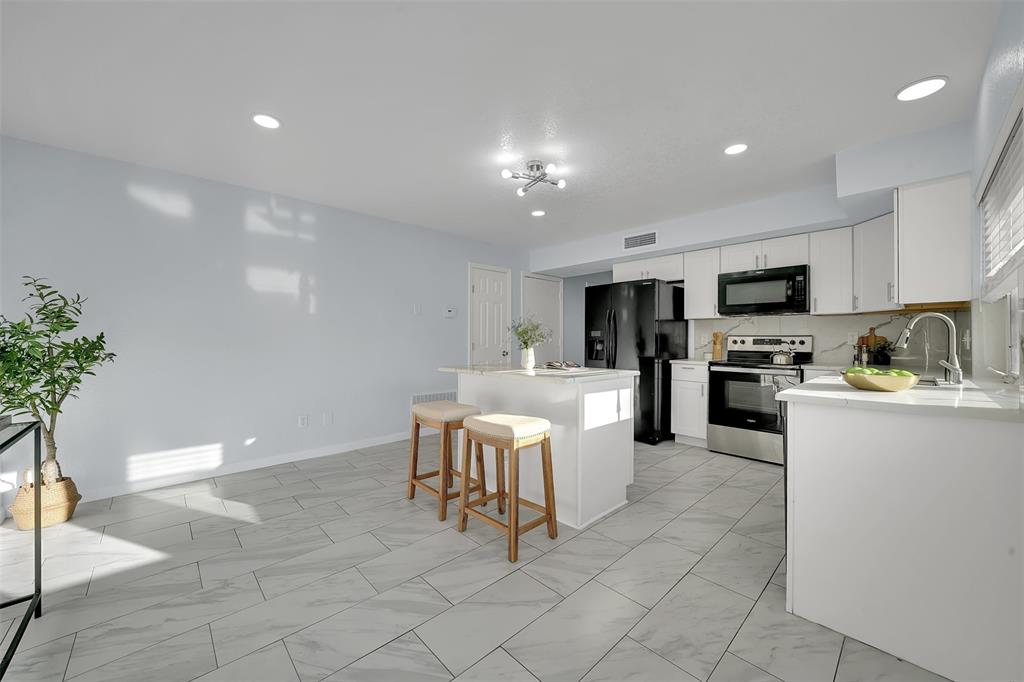1024 East Peters Colony Road Carrollton, TX 75007 - Photo 15 of 38 Kitchen with black appliances, white cabinetry, a kitchen island, a breakfast bar area, and light marble finish floors