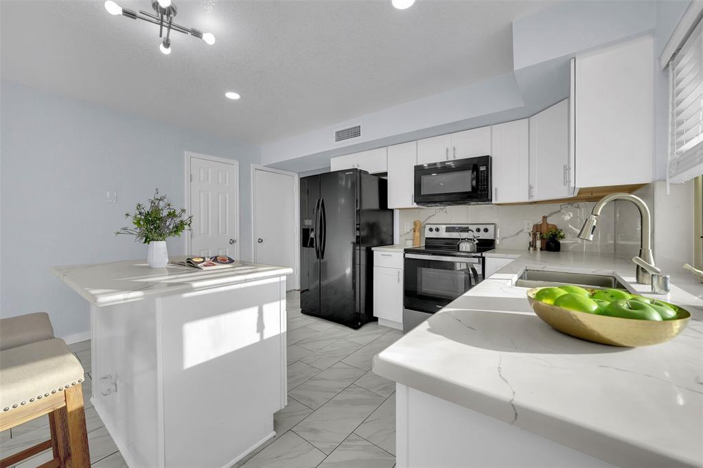 1024 East Peters Colony Road Carrollton, TX 75007 - Photo 19 of 38 Kitchen featuring black appliances, white cabinetry, a center island, light stone counters, and backsplash