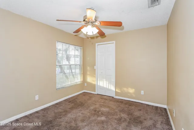 an empty room with chandelier fan and windows