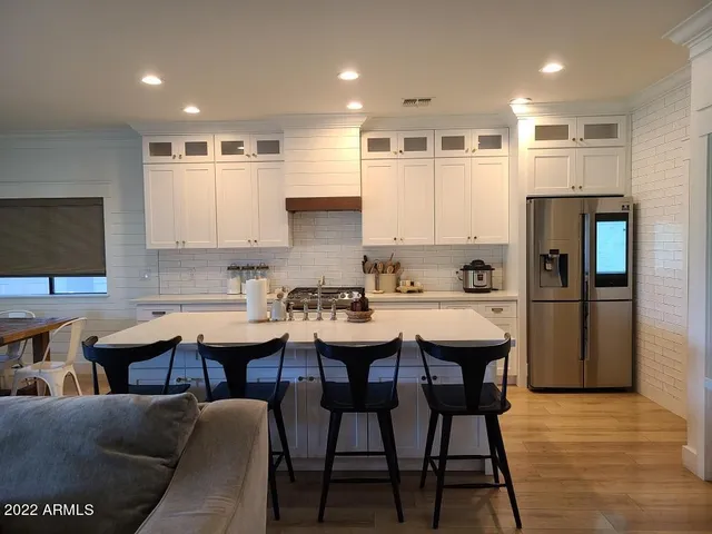 a kitchen with stainless steel appliances kitchen island granite countertop a sink a stove a refrigerator and white cabinets with wooden floor