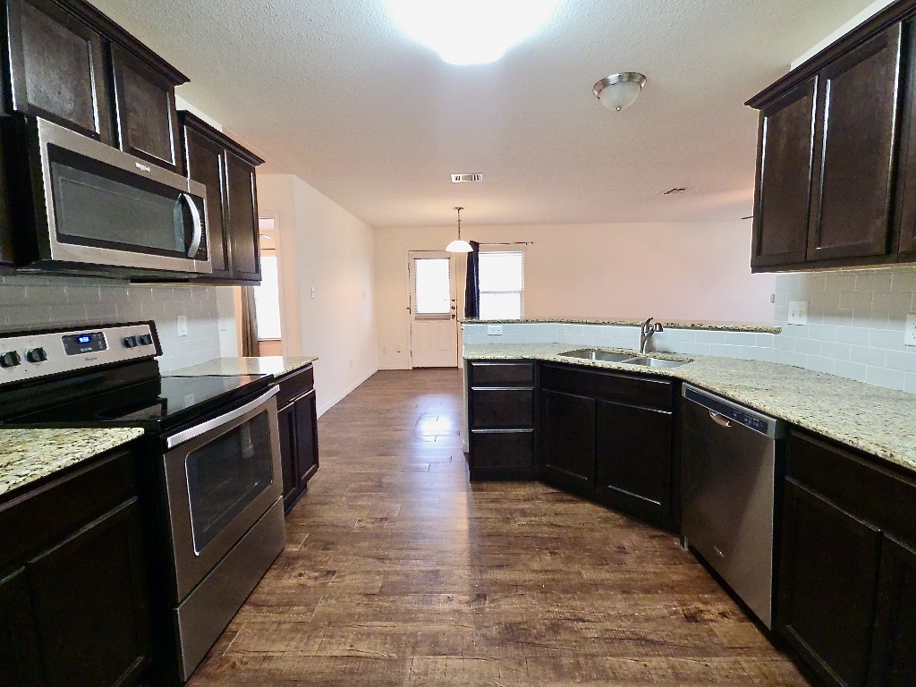 306 Wyeth Street Taylor, TX 76574 - Photo 4 of 20 Kitchen with dark cabinetry, granite countertops, stainless steel appliances and laminate flooring.