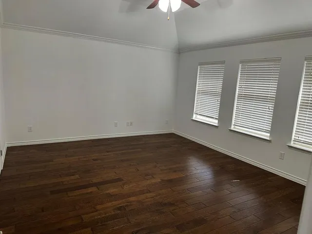 an empty room with wooden floor chandelier fan and windows